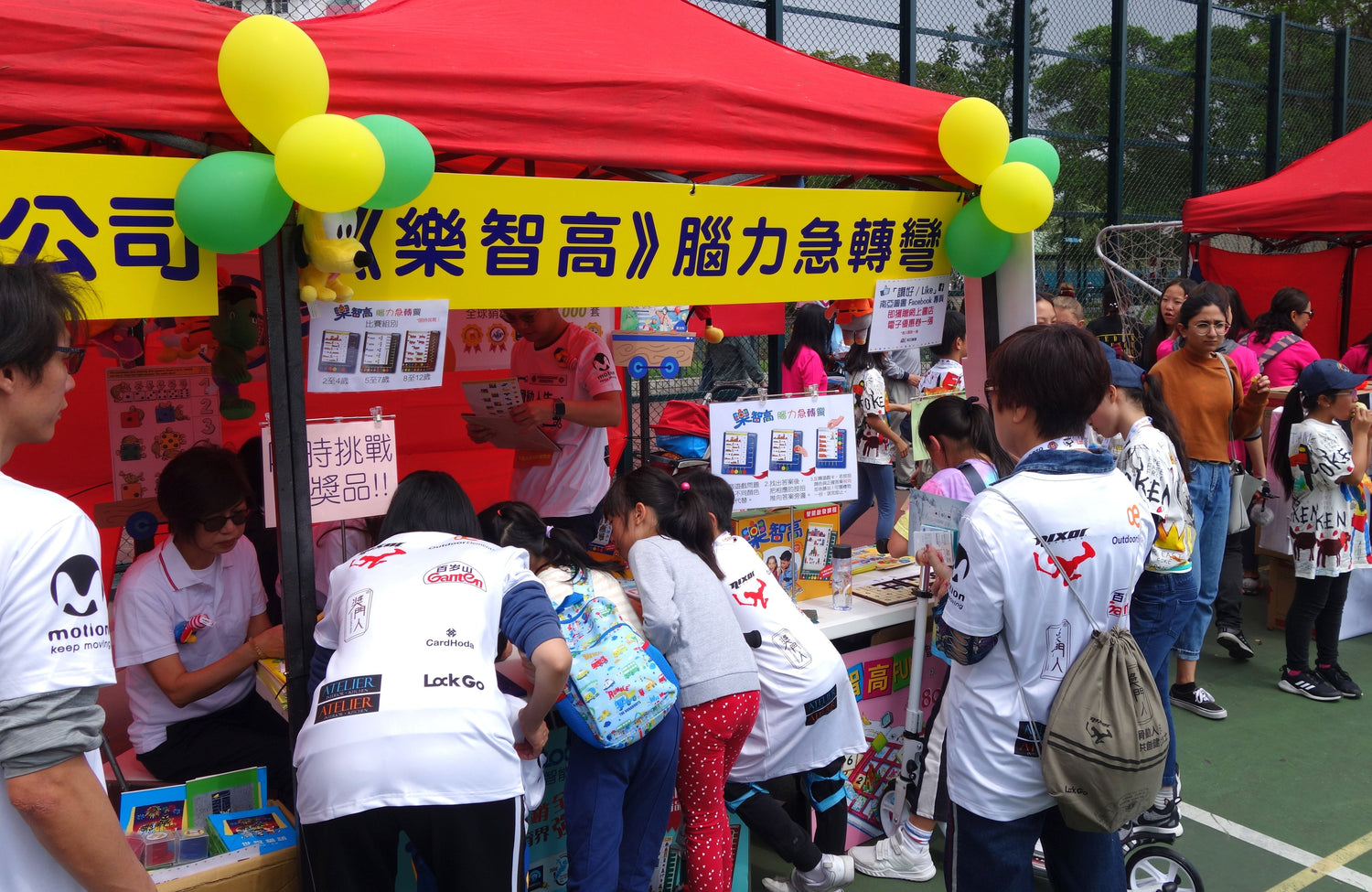Children and adults at an outdoor educational booth with games, books, and colorful displays