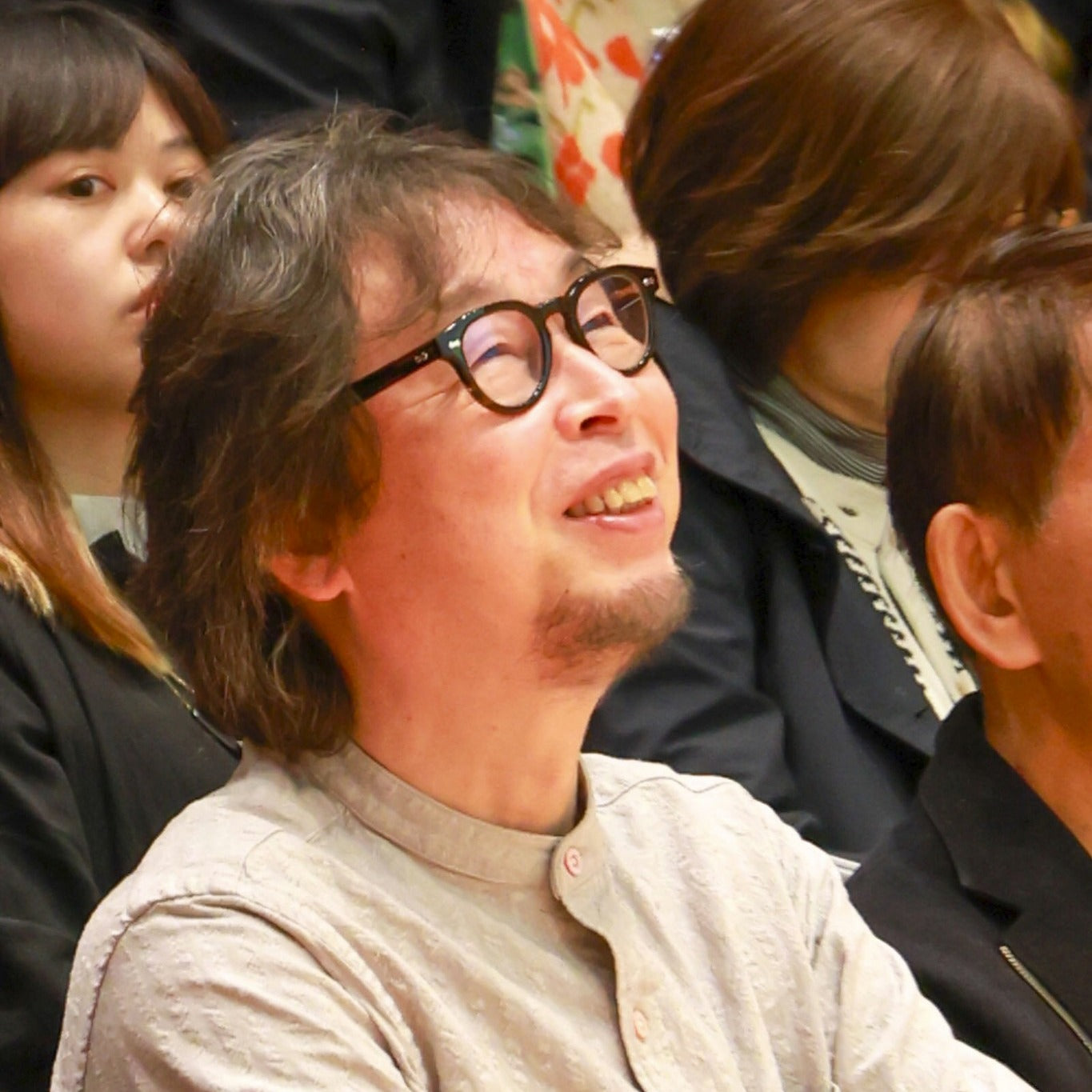 Asian man with glasses smiling in audience at an indoor educational event