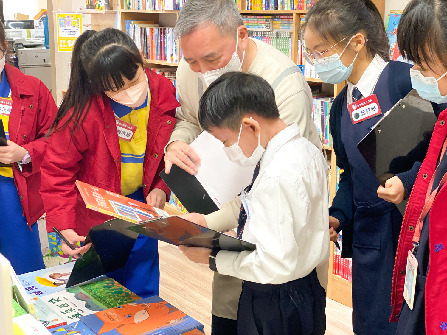 Children and a teacher browsing educational picture books in a bookstore, all wearing masks.