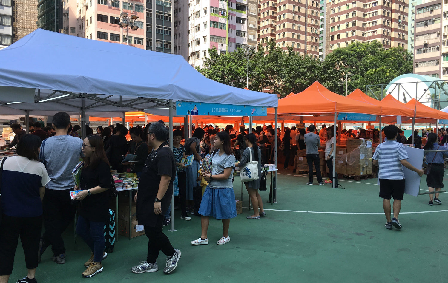 Crowd browsing books at outdoor book fair with colorful tents in urban city setting