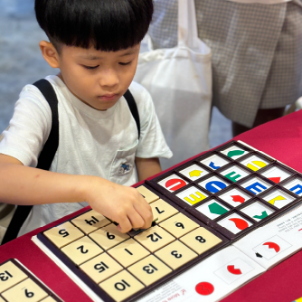 一位小男孩在活動體驗區，正認真地將數字方塊放入智高FUN遊戲板中。