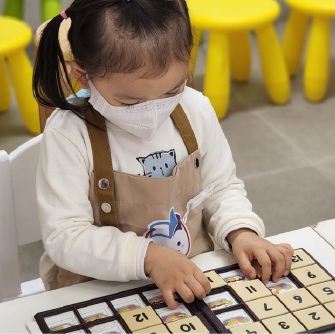 一位穿著背帶褲的小女孩，在黃色椅子上專心地玩著智高FUN遊戲板。