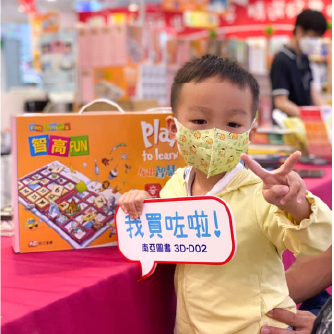 一位戴著口罩的小男孩在智高FUN的攤位前，高興地做出勝利手勢。