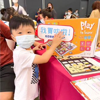 一位戴著口罩的小男孩在智高FUN的攤位前，高興地做出勝利手勢。