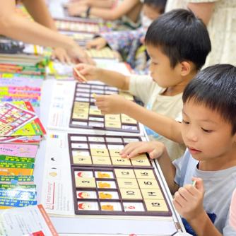 兩位小男孩在書展攤位上並肩坐著，一起投入地玩智高FUN遊戲板。