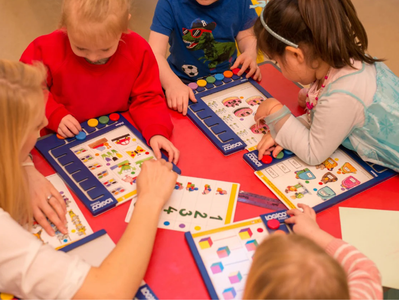 A group of young children gathered around a table, learning together with LOGICO.
